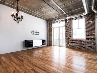 Unfurnished living room featuring brick wall, wood finished floors, and a chandelier