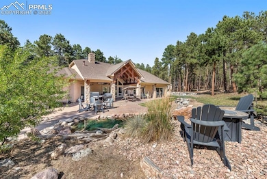 Rear view of property with an outdoor fire pit, a chimney, a patio, a shingled roof, and stone siding