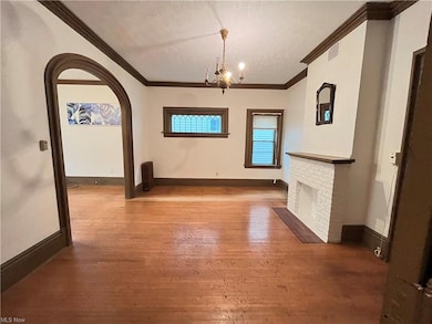 Unfurnished living room with a notable chandelier, a brick fireplace, ornamental molding, and light hardwood flooring