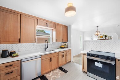 Kitchen featuring stainless steel appliances, decorative backsplash, decorative light fixtures, light brown cabinetry, and light stone countertops