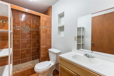 Primary Bathroom - The bathroom adjacent to the primary bedroom features warm wood-patterned tiles with a decorative mosaic accent in the shower area. The vanity has a simple white countertop, offering functionality and style in a compact space.
