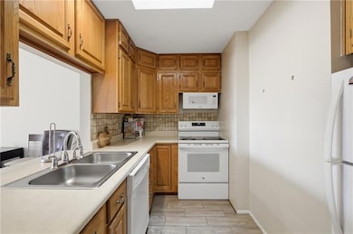 Kitchen featuring white appliances, light countertops, brown cabinetry, wood tiled floors, and backsplash