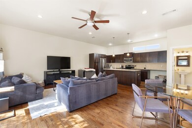 Living room with ceiling fan, wood finished floors, open to kitchen and dining area.