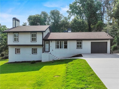 Tri-level home with a chimney, brick siding, an attached garage, and a front lawn
