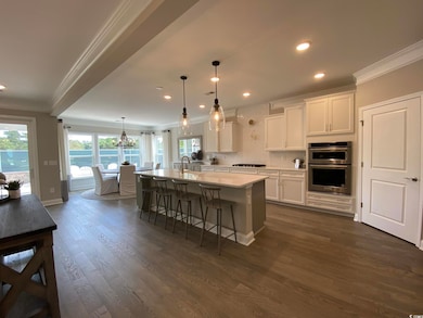 Kitchen with ornamental molding, double oven, white cabinets, gas cooktop, and a breakfast bar