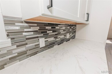 Kitchen view of white cabinetry, tasteful backsplash, and light stone counters