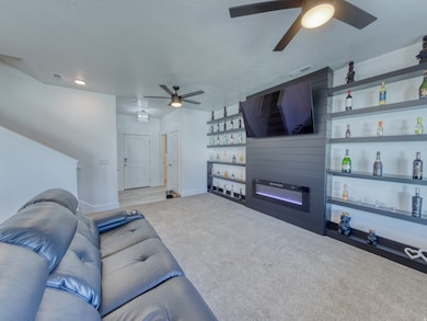 Living area with ceiling fan, a large fireplace, carpet flooring,.