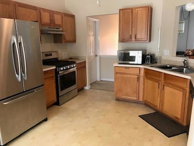 Kitchen with appliances with stainless steel finishes, under cabinet range hood, a sink, light countertops, and brown cabinetry