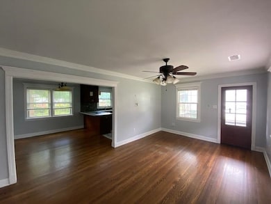 Unfurnished living room featuring crown molding, dark wood-style floors, and a ceiling fan