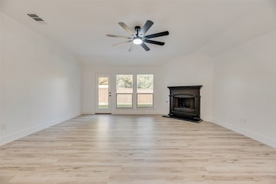 Unfurnished living room with light wood finished floors, a fireplace with raised hearth, and a ceiling fan