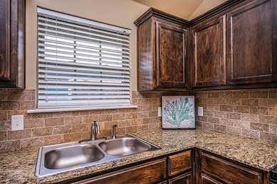 Kitchen with dark brown cabinets, decorative backsplash, and dark stone counters