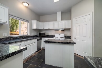 Kitchen featuring white cabinetry, appliances with stainless steel finishes, stone tile floors, and dark stone countertops