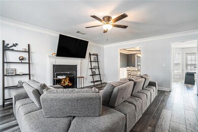 Living area featuring a ceiling fan, ornamental molding, dark wood-style floors, and a lit fireplace