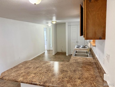 Kitchen with a peninsula, a textured ceiling, white range with electric stovetop, dark countertops, and brown cabinets