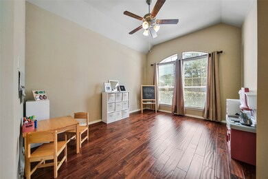 The study/play room features gleaming wood floors, a vaulted ceiling, a ceiling fan, and large windows with lush views of the front lawn. Blinds are included throughout the home for privacy and lighting control.