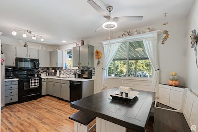 Kitchen featuring light countertops, black appliances, decorative backsplash, light wood finished floors, and gray cabinetry