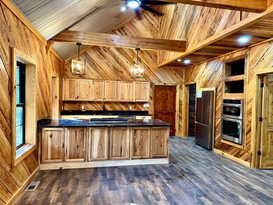 Kitchen featuring wooden walls, dark countertops, appliances with stainless steel finishes, a peninsula, and dark wood-style flooring