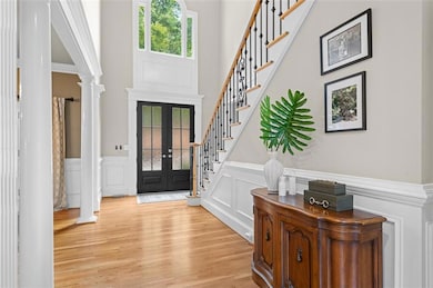 Entrance foyer featuring decorative columns, a high ceiling, light wood-style flooring, a decorative wall, and wainscoting