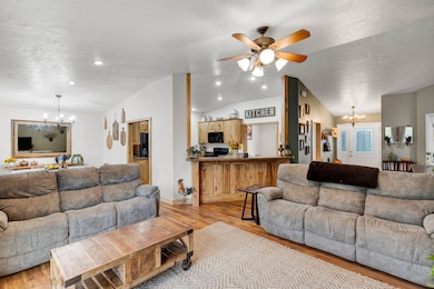Living area featuring a chandelier, ceiling fan, light wood finished floors, vaulted ceiling, and a textured ceiling