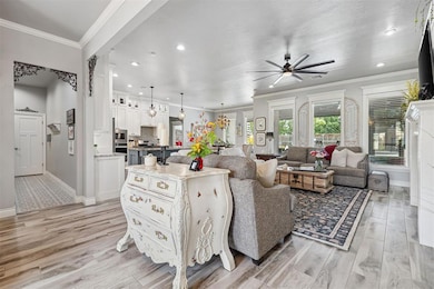 Living area featuring a ceiling fan, baseboards, recessed lighting, light wood-style floors, and crown molding