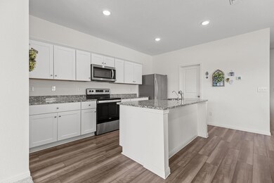 Kitchen with stainless steel appliances, white cabinets, light stone countertops, a kitchen island with sink, and dark wood-style flooring