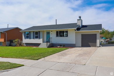 Single story home featuring a chimney, driveway, brick siding, a garage, and a front yard