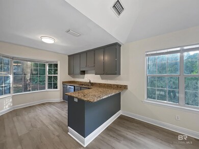 Kitchen with light wood-type flooring, a peninsula, gray cabinetry, and dark stone counters