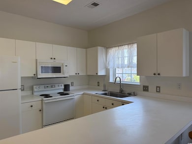 Kitchen with white appliances, a sink, light countertops, and white cabinets