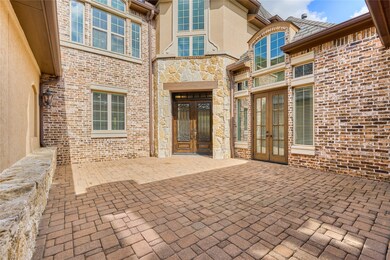 A beautiful courtyard invites you into this stunning home.Courtyard with a brick and stone facade, large windows, and a decorative wooden door. The area is paved with interlocking bricks, offering a charming and low-maintenance outdoor space.