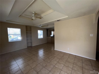 Empty room featuring light tile patterned flooring, built in shelves, a ceiling fan, a tray ceiling, and arched walkways