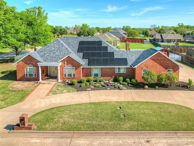 View of front facade featuring a front lawn, a shingled roof, solar panels, and brick siding