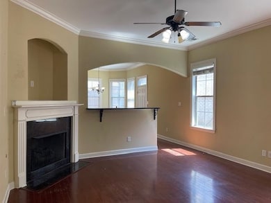 Unfurnished living room with dark wood-type flooring, ornamental molding, a fireplace with flush hearth, and a ceiling fan
