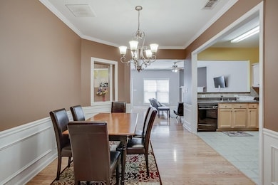 Dining area featuring a chandelier, ornamental molding, a ceiling fan, light wood-style flooring, and wainscoting