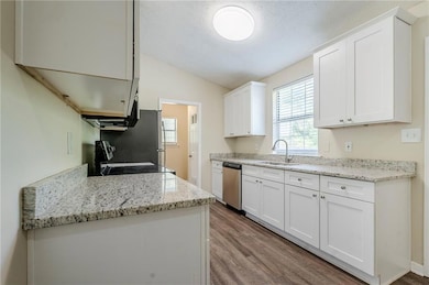 Kitchen with dishwasher, a sink, wood finished floors, range, and lofted ceiling