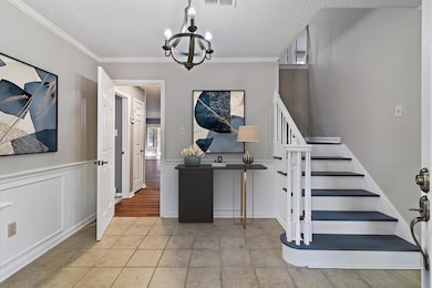 Stairs with ornamental molding, tile patterned floors, a textured ceiling, wainscoting, and a chandelier