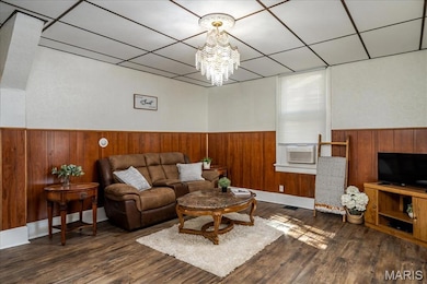 Main floor Living room featuring dark wood-style floors, a drop ceiling, a wainscoted wall, and a chandelier