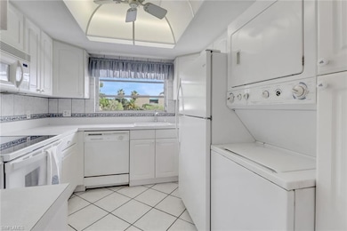 Kitchen featuring stacked washer / drying machine, white appliances, ceiling fan, white cabinets, and light countertops