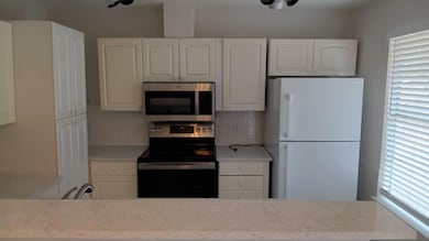 Kitchen featuring electric range oven, freestanding refrigerator, stainless steel microwave, backsplash, and white cabinetry