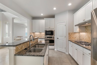 Kitchen with a sink, appliances with stainless steel finishes, under cabinet range hood, light tile patterned floors, and a kitchen island with sink