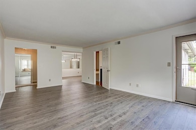 Unfurnished living room with crown molding, plenty of natural light, wood finished floors, baseboards, and a chandelier