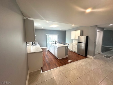 Kitchen with white cabinets, dark tile patterned floors, freestanding refrigerator, recessed lighting, and a center island with sink
