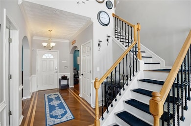Entryway with a chandelier, dark wood-style floors, ornamental molding, arched walkways, and a textured ceiling