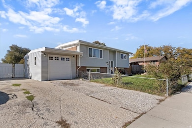 Raised ranch featuring a fenced front yard, concrete driveway, and a garage
