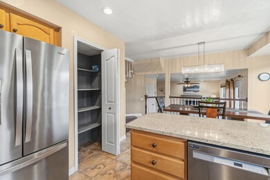 Kitchen featuring appliances with stainless steel finishes, light stone countertops, brown cabinets, hanging light fixtures, and open floor plan