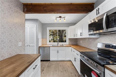 Kitchen with butcher block countertops, appliances with stainless steel finishes, white cabinets, light wood finished floors, and beamed ceiling