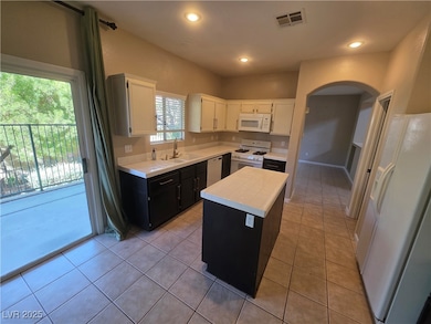 Kitchen with tile counters, white appliances, a center island, light tile patterned floors, and dark cabinets