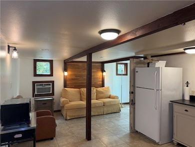 Living room featuring plenty of natural light, a textured ceiling, beam ceiling, light tile patterned floors, and a wall mounted air conditioner