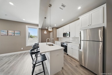Kitchen with appliances with stainless steel finishes, tasteful backsplash, a breakfast bar area, white cabinetry, and recessed lighting