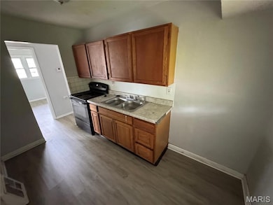 Kitchen featuring black electric range, brown cabinetry, light countertops, dark wood finished floors, and backsplash