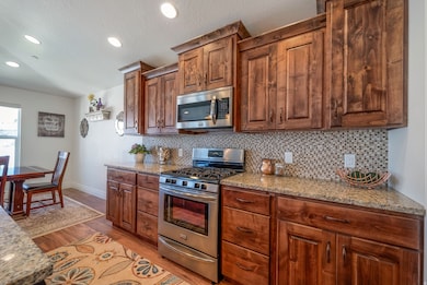 Kitchen featuring stainless steel appliances, light stone counters, backsplash, light wood finished floors, and recessed lighting